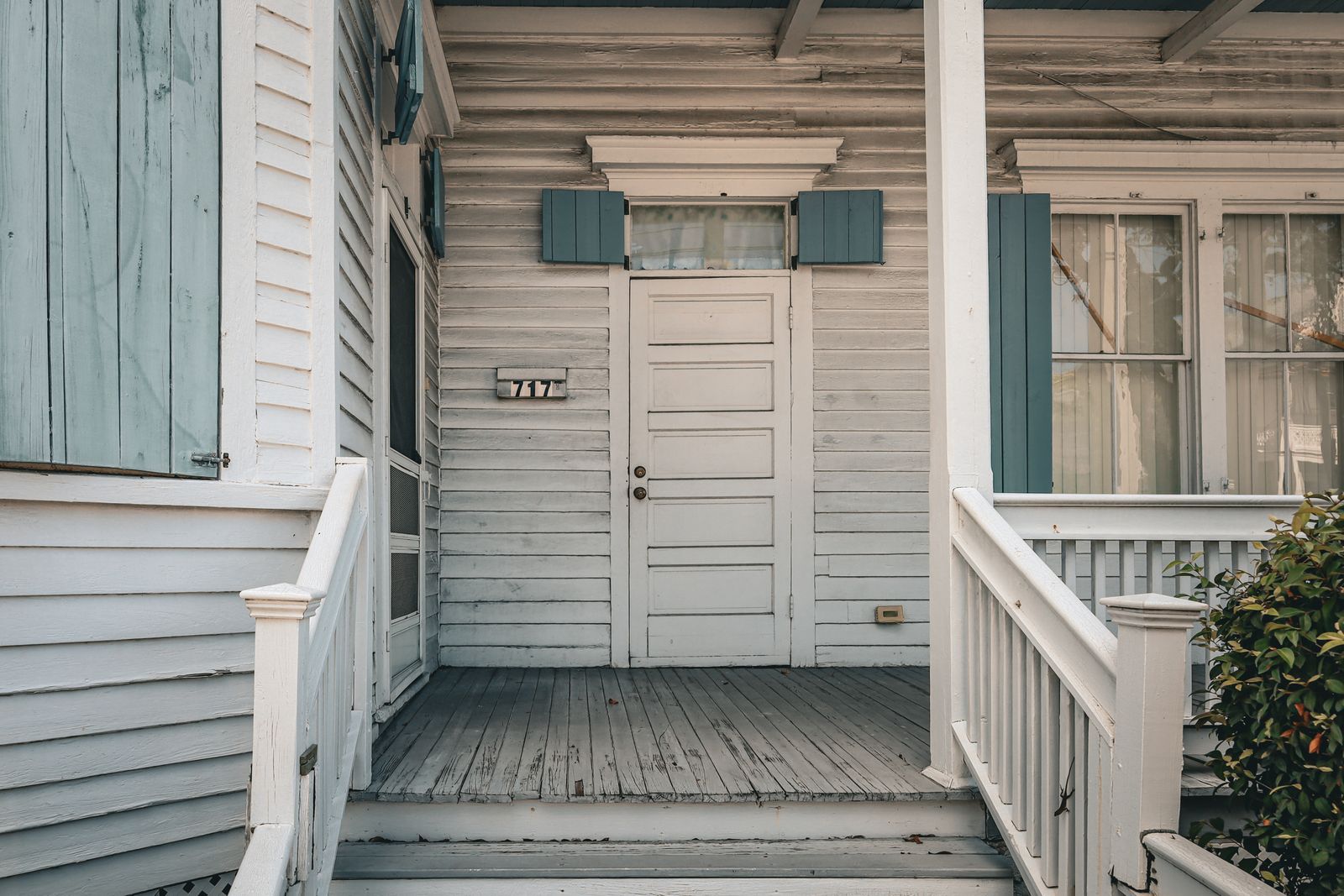 An older white wooden house with weathered siding and blue shutters, ready to be repainted