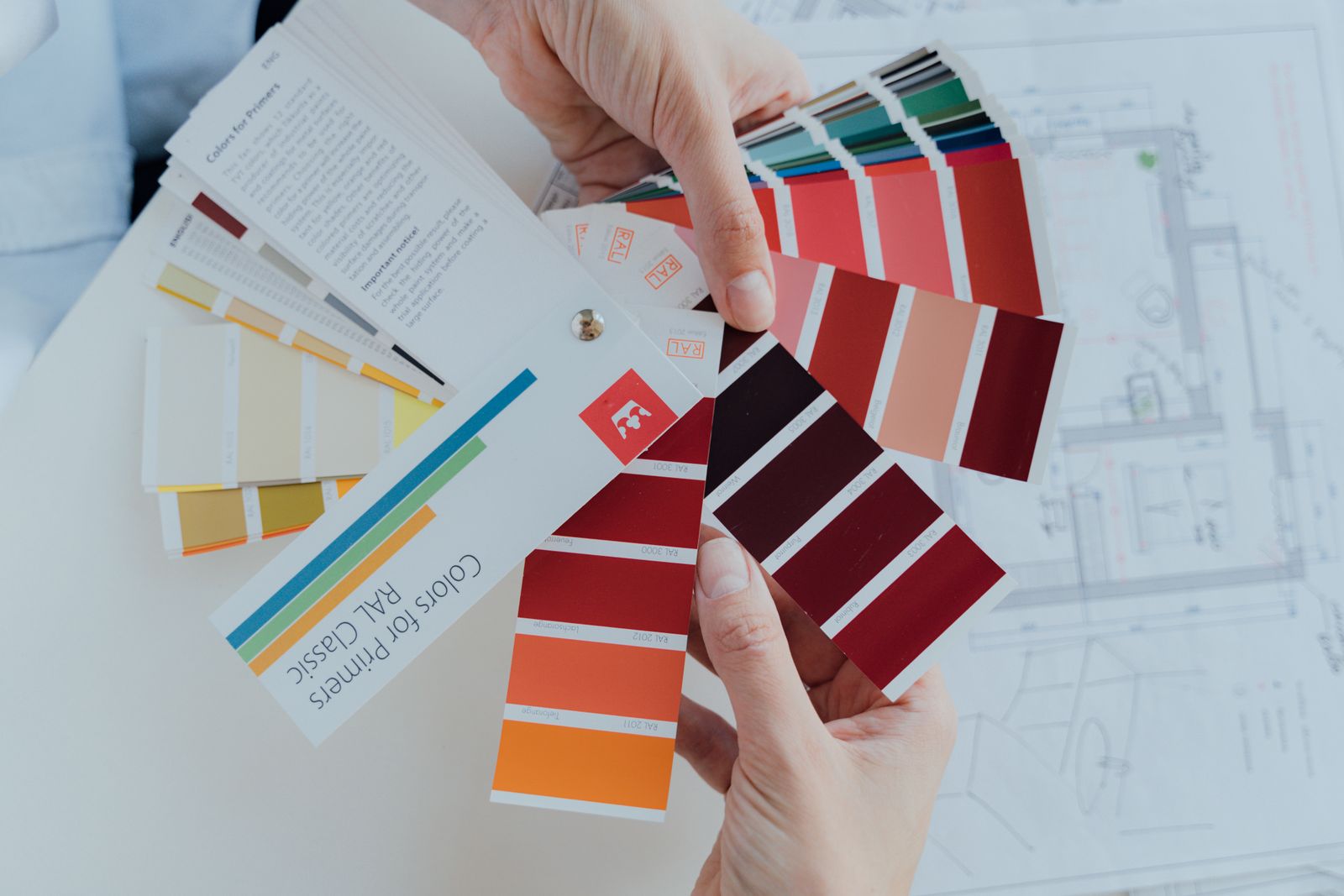 Hands holding paint color swatches over a set of house plans