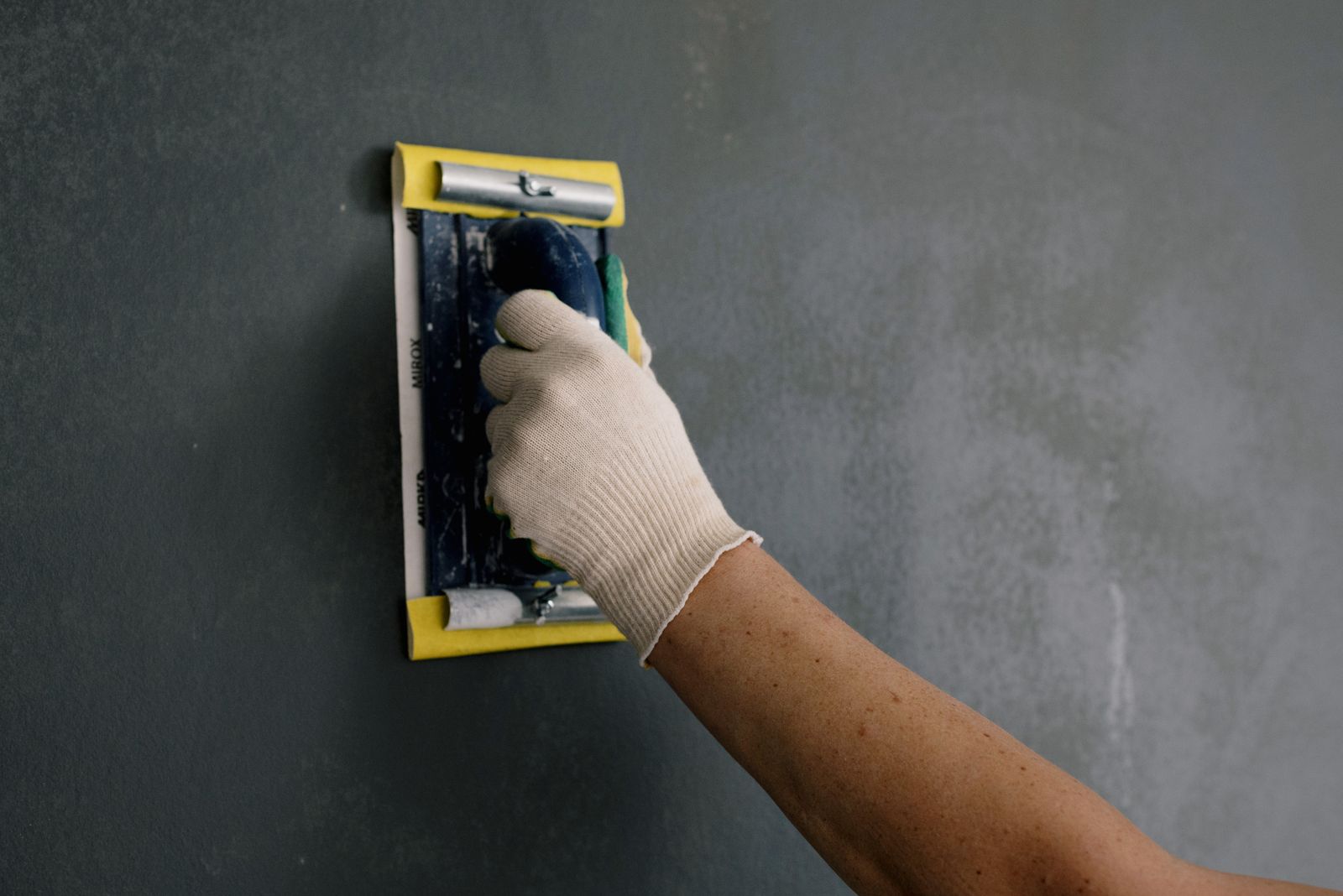 A gloved hand sanding a freshly filled and smoothed wall